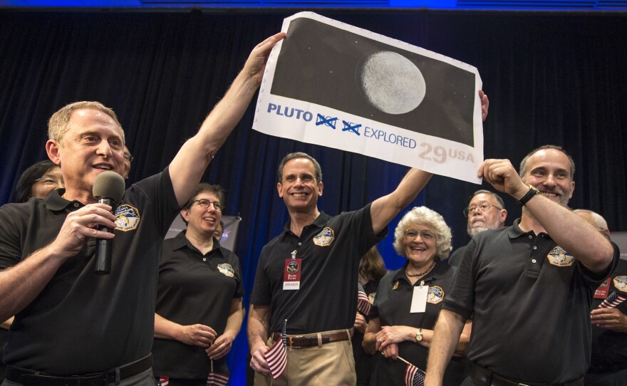 Members of the New Horizons team celebrated last year with a blown up image of the postage stamp when the probe made its closest approach to Pluto.