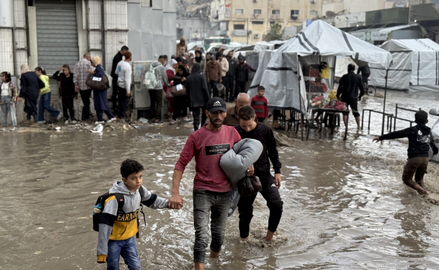 A father and his son wade through flooded streets in Gaza City after picking up humanitarian aid on Nov. 25, 2025.