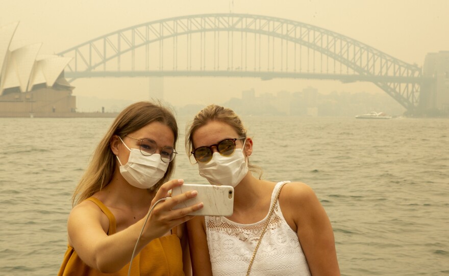 Tourists, wearing face masks due to heavy smoke, take a selfie at Sydney Harbour on Dec. 19, 2019. As news of Australia's wildfires spreads around the world, fewer tourists are arriving in the country.