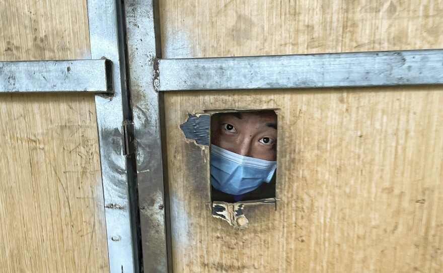 A resident looks through a hole from inside a locked-down area in Beijing on June 30, 2022. China implemented a "zero-COVID" policy that was disorienting and disruptive for global companies.