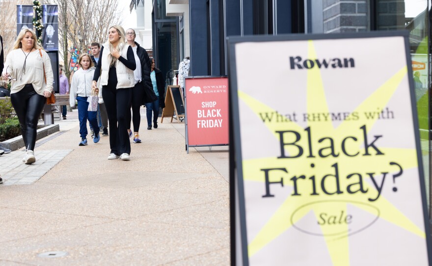 Shoppers walk past sale signs at the Avalon shopping center in Alpharetta, Ga., during Black Friday in 2022.