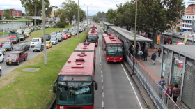 Transmilenio's rapid buses enter and exit a rail-like raised platform beside a snake of traffic on the left. 