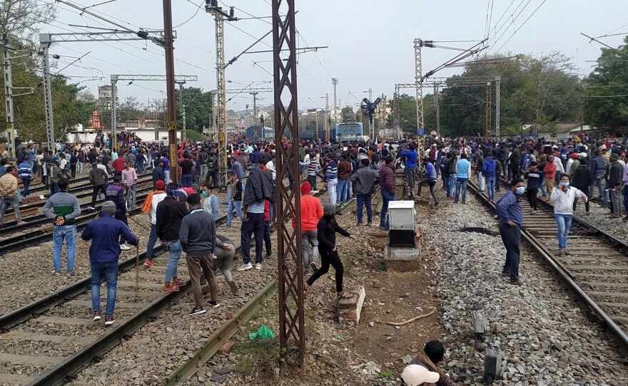 People gather near a train set on fire by a mob in Gaya protesting the restrictive qualifications set for railway jobs.