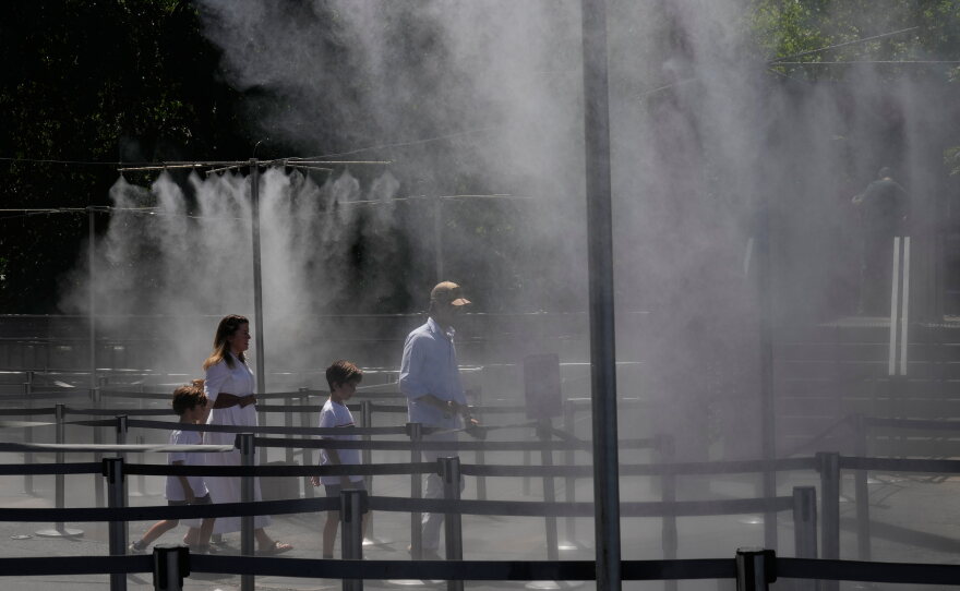 A family walks through a cooling water spray at the Eiffel Tower in Paris, Sunday, June 21, 2026.