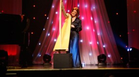 Promotional photo of singer/harpist Orla Fallon performing on stage and playing the harp. 