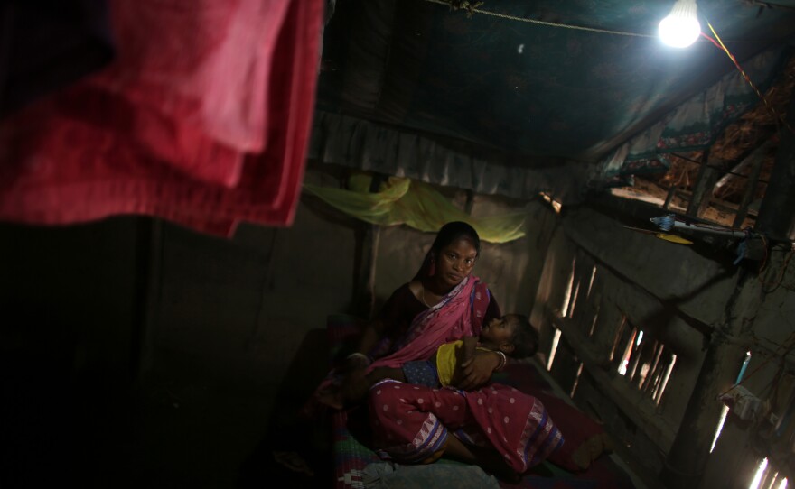 Arati Sardar sits in her house with baby Sridoy. One of the family's goats was taken and eaten by a tiger, but having electricity now helps keep the home safer.