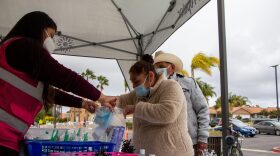 Lilian Serrano helps Maria Roja bag face masks and rapid COVID-19 tests outside of a vaccine clinic at La Mirada Academy in San Marcos, Calif. in this undated photo. 