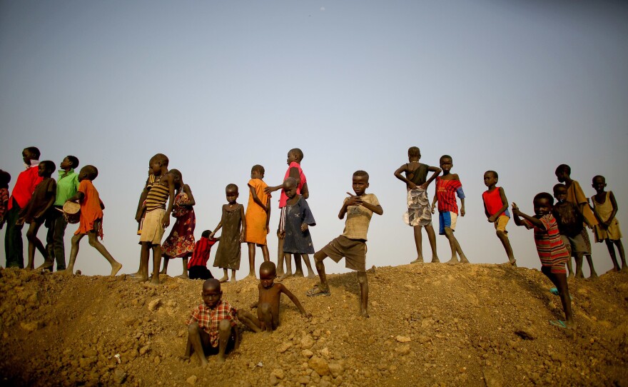 The earthen wall that the children are standing on forms one side of a massive water retention pond in the middle of the camp.