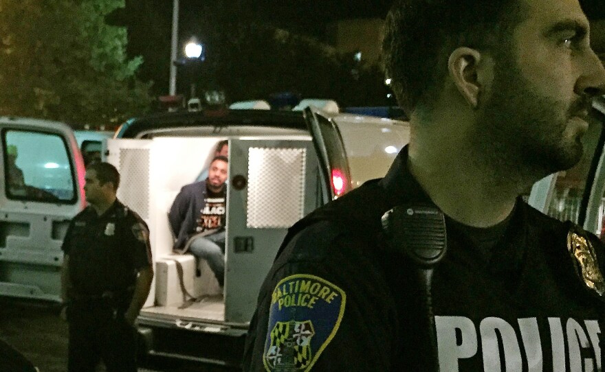 Police stand near vans holding protesters early Thursday in Baltimore.