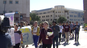 A group of about two dozen students holding signs protest through Cal State San Marcos' campus. 