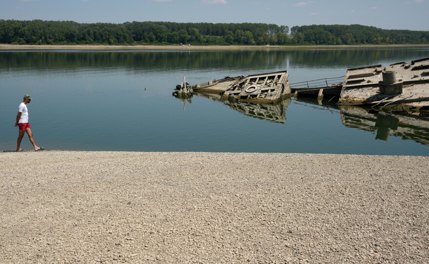 A man walks on a sandbank by the wreckage of a WWII German warship, which emerged during the drought in front of Djerdap II, a large dam on the Danube River between Romania and Serbia near Prahovo on Aug. 4, 2026.