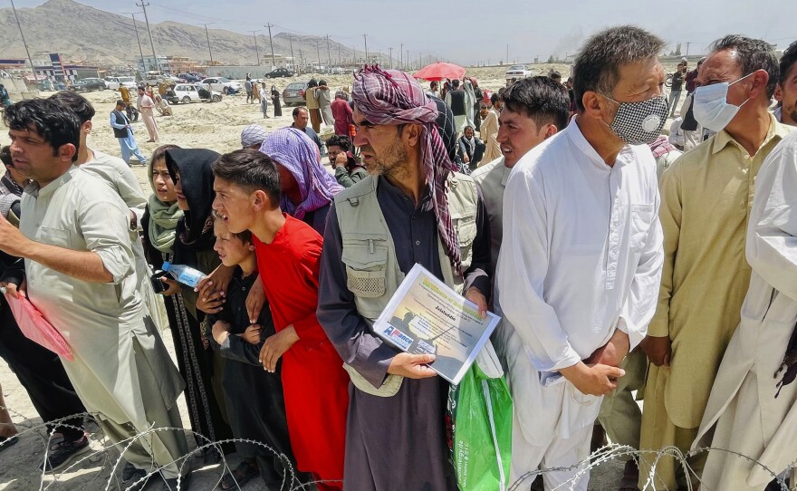A man holds a certificate acknowledging his work for Americans as hundreds of people gather outside the international airport in Kabul, Afghanistan, Tuesday, Aug. 17, 2021.