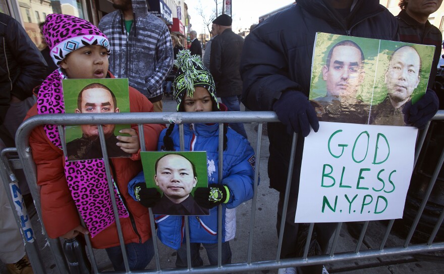 People hold up photographs of officers Rafael Ramos and Wenjian Liu as the casket of Ramos arrives for his wake.