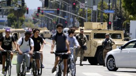 Cyclists ride down a street past a road block with National Guard troops along Ocean boulevard in Santa Monica, Calif. on Sunday June 7, 2020. 