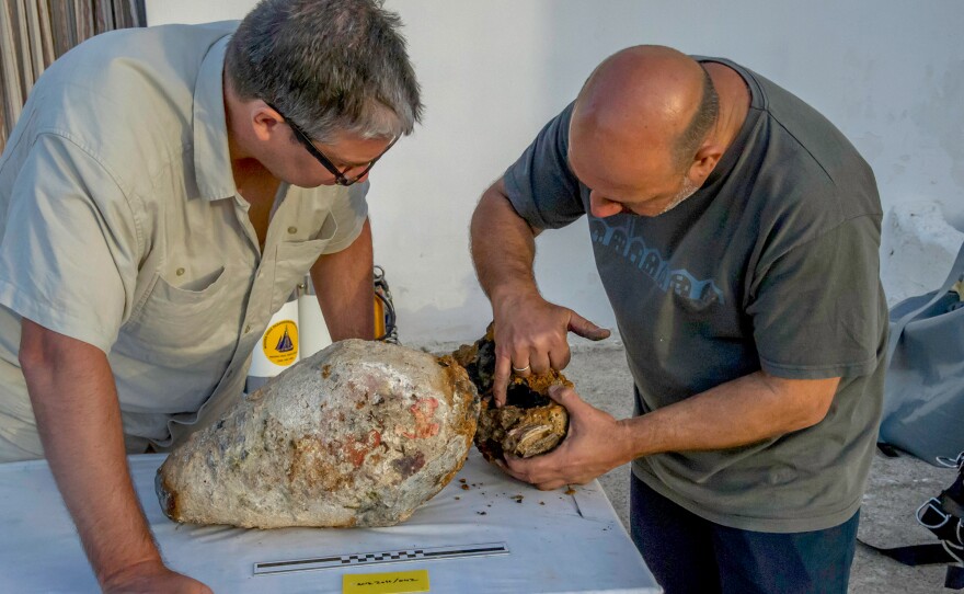 Project co-directors Brendan Foley and Theotokis Theodoulou inspect the torpedo-shaped lead cylinder recovered from the Antikythera shipwreck.
