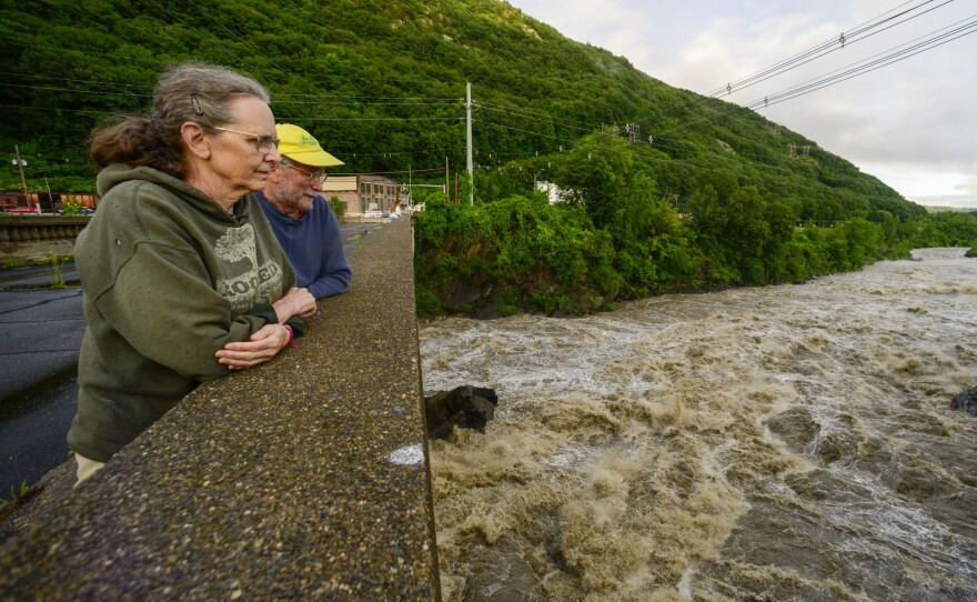 People stand on the Vilas Bridge, in Bellows Falls, Rockingham, Vt., to watch the water from the Connecticut River flow through on Monday, July 10, 2023. Heavy rain has washed out roads and forced evacuations in the Northeast, especially in Vermont and New York.