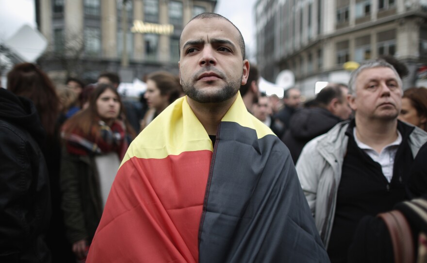 A man wears the Belgian flag as people observe a one minute silence Wednesday at the Place De La Bourse, in honor of the victims of Tuesday's terror attacks in Brussels.