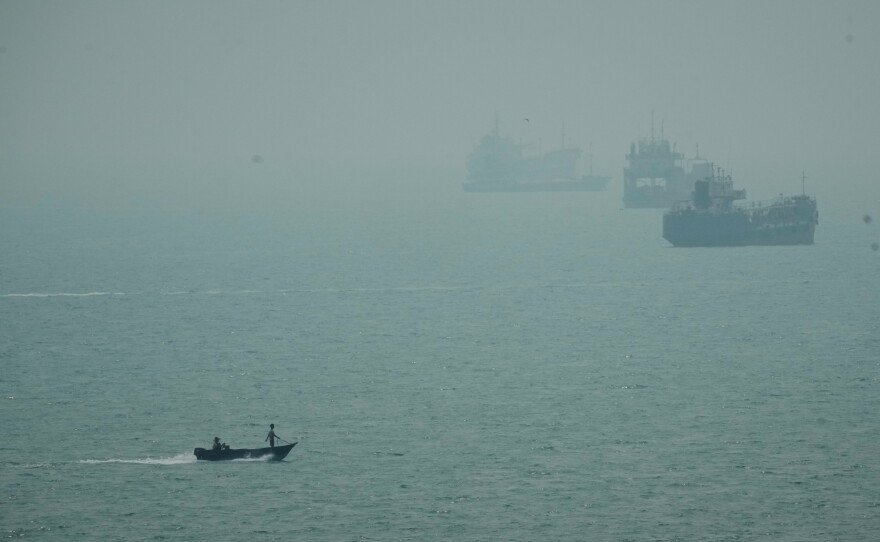 A motorboat travels past commercial vessels anchored amid haze in the Strait of Hormuz off Bandar Abbas, Iran, Monday, Sept. 7, 2026.