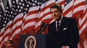 President Ronald Wilson Reagan at the podium with American flags lining the background. 