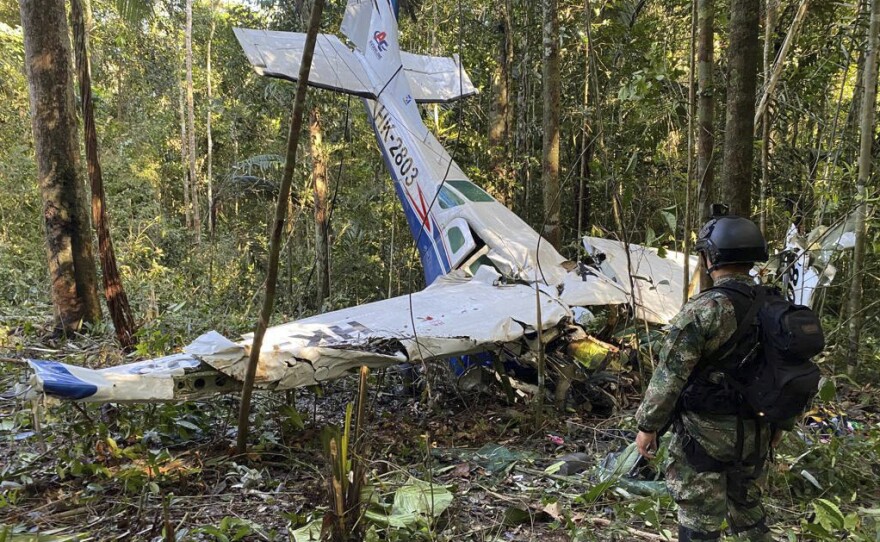 In this photo released by Colombia's Armed Forces Press Office, a soldier stands in front of the wreckage of a Cessna C206, May 18, 2023, that crashed in the jungle of Solano in the Caqueta state of Colombia. The discovery of footprints on May 30 of a small foot rekindled the hope of finding the children alive after their plane crashed on May 1.