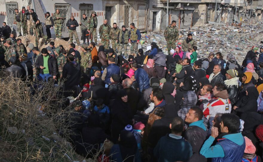 Syrian residents fleeing violence gather at a checkpoint, manned by pro-government forces, in the Maysaloun neighborhood of Aleppo on Thursday.