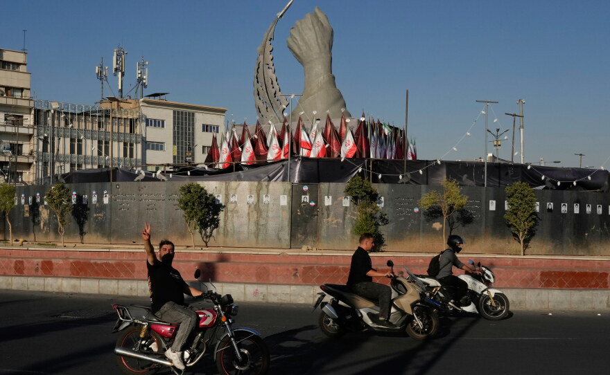 A man reacts to the camera while driving past a monument depicting the clenched fist of the late Iranian Supreme Leader Ayatollah Ali Khamenei, who was killed in U.S. and Israeli strikes on Feb. 28, and a missile at the Islamic Revolution square in downtown Tehran, Iran, Tuesday.