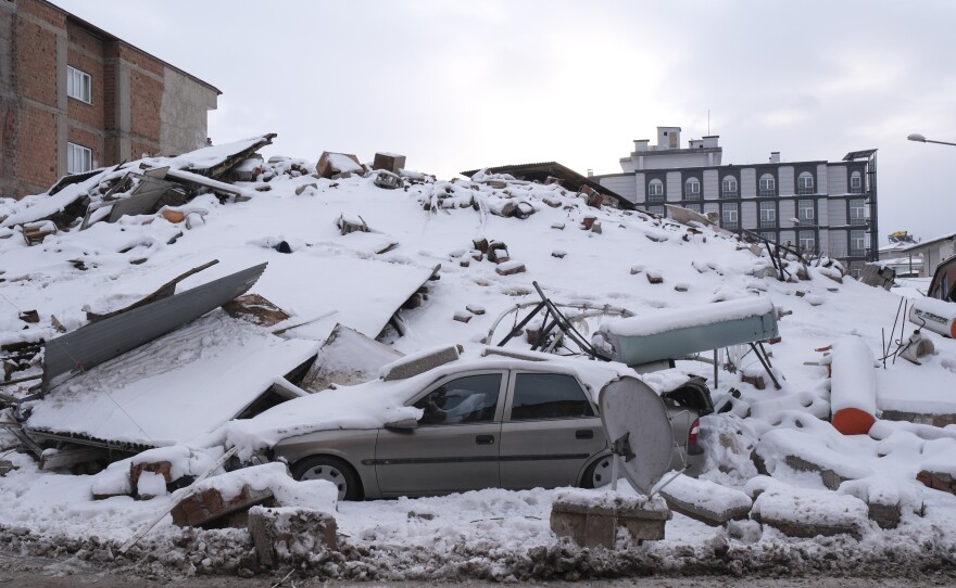 A collapsed building and a car are covered in snow in Elbistan, Turkey.