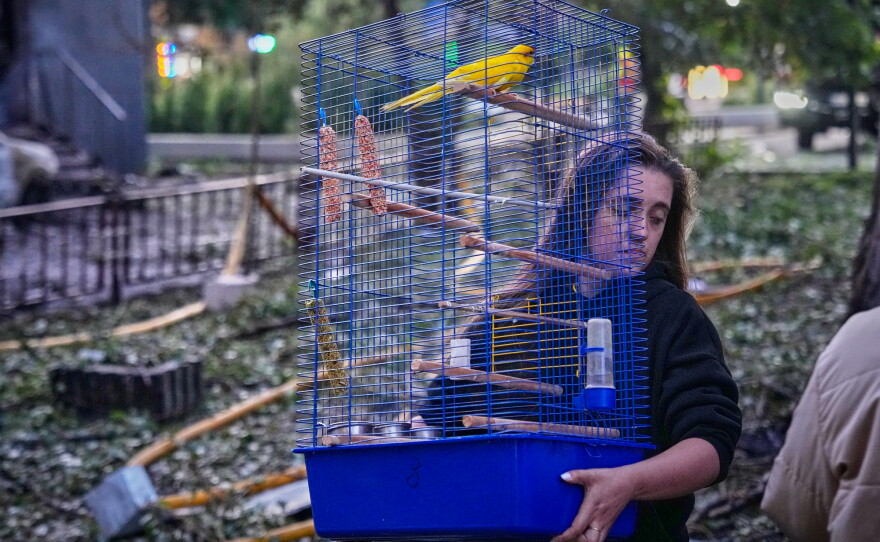A woman carries a cage with a parrot as she leaves her damaged house following a Russia missile attack in Kyiv, Ukraine, Sunday, July 19, 2026.