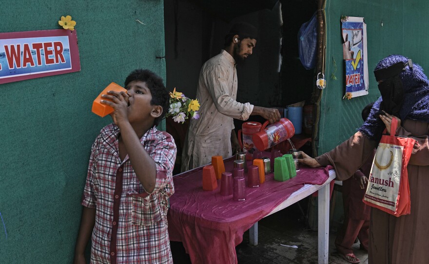 A volunteer distributes drinking water next to a bus stand on a hot summer day in Hyderabad, India, Thursday, March 21, 2024.