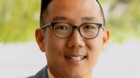 photo of Alex Kim, wearing blue blazer, a colorful, striped tie, and glasses