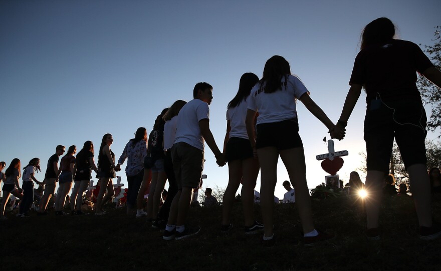 Students and family members hold hands around a makeshift memorial in front of Marjory Stoneman Douglas High School in Parkland, Fla., where 17 people were killed on Feb. 14.