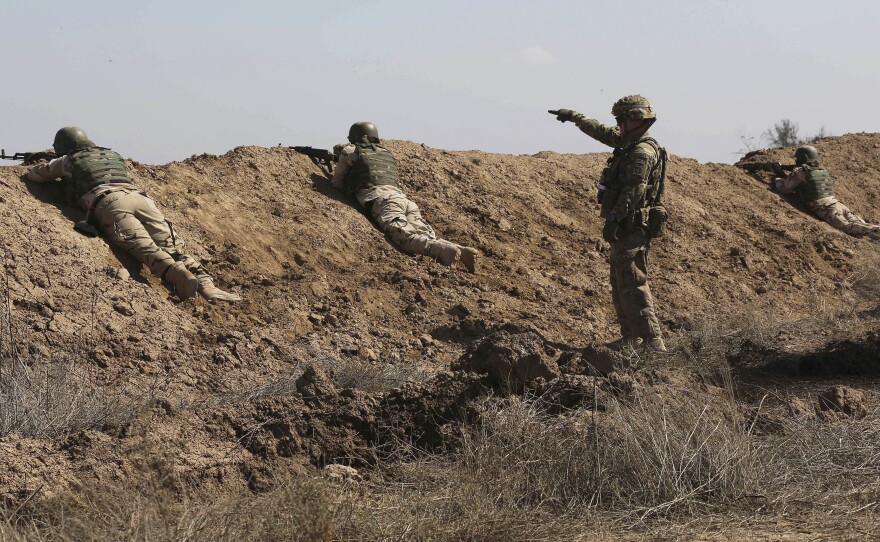 A U.S. soldier (standing) helps Iraqi security forces improve shooting skills at Camp Taji, north of Baghdad, in 2015.