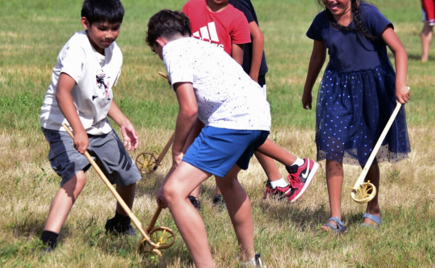 A group of children from different tribal nations play lacrosse together using traditional equipment.