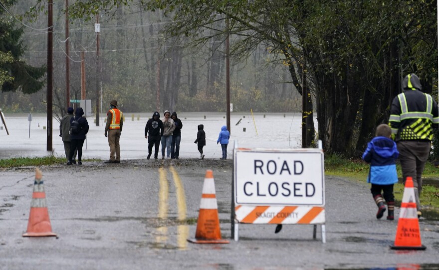 Local residents walk up to a flooded roadway in Sedro-Woolley, Wash., on Monday.