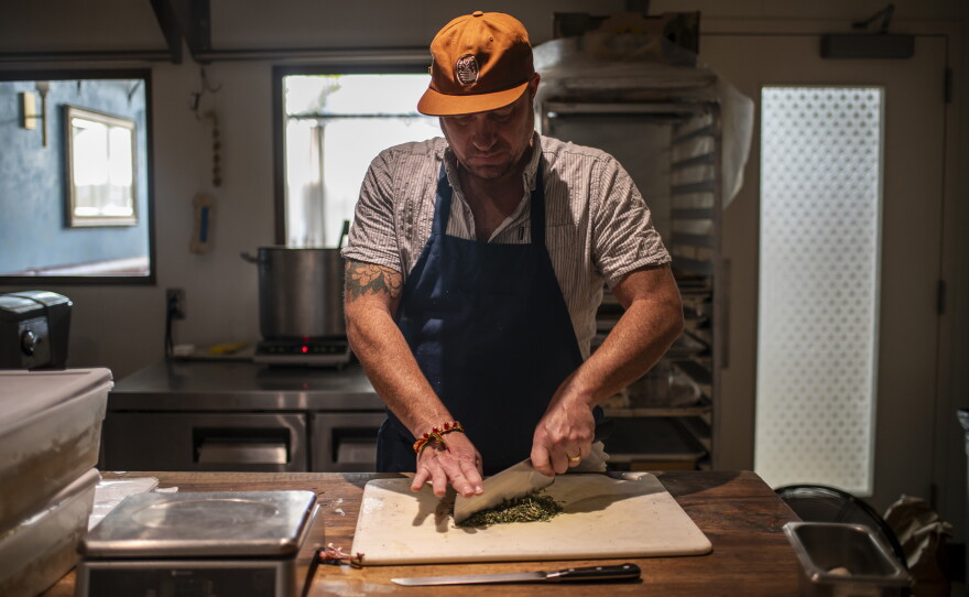 Tedesco chops rosemary in the kitchen. He hopes the pay-what-you-will promotion can be a way to meet the current affordability and social challenges facing Americans.