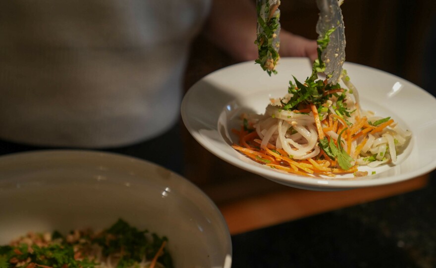 Adler tosses the peanut butter sauce with rice noodles and various veggies.