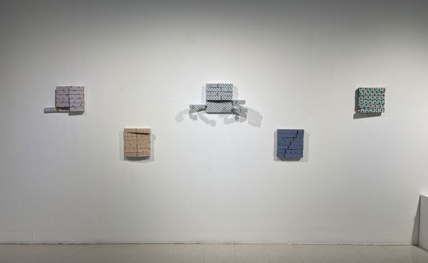Five small canvases are arranged on a wall. Each canvas is actually a series of small, rib- or limb-like canvases made from patterned hospital gowns, with the pieces attached on hinges and movable. The middle canvas resembles an opened-up rib cage.