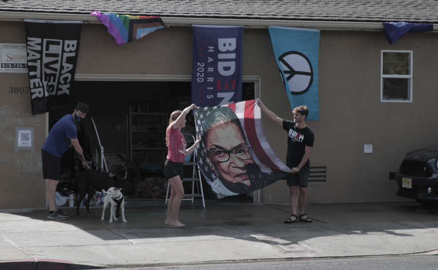 Normal Heights residents Mary Calhoun (left) and Barrett Pall (right) celebrate Biden's presidential win by waving a flag of Ruth Bader Ginsberg, in this photo taken Nov. 7, 2020.