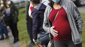  In this May 7, 2020 file photo, a pregnant woman wearing a face mask and gloves holds her belly as she waits in line for groceries at St. Mary's Church in Waltham, Mass.