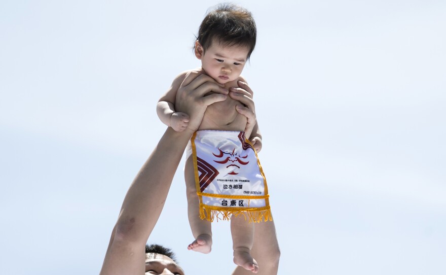 The number of babies born in Japan fell an estimated 5.9% this year, to under 900,000. Here, a baby is held aloft by a sumo wrestler during Tokyo's Nakizumo Festival in April.