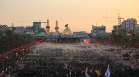 Large crowds of pilgrims fill the area between the two holy shrines in Karbala at sunset, with the illuminated dome and minarets of Imam Hussein's shrine visible in the background during the Arbaeen commemoration.