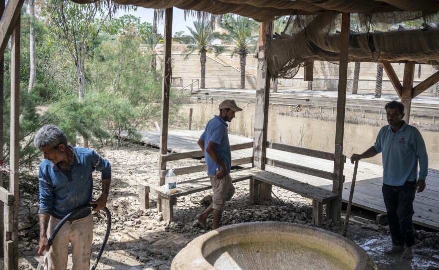 Jordanian workers at Jordan's baptism site cleaning up after a recent flood. The marble font is used for baptizing infants who cannot be baptized in the river. The site has been closed to visitors since mid-March due to the coronavirus pandemic and parts of the site have been sterilized.