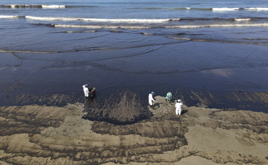 Workers clean up oil from Cavero beach on Tuesday.