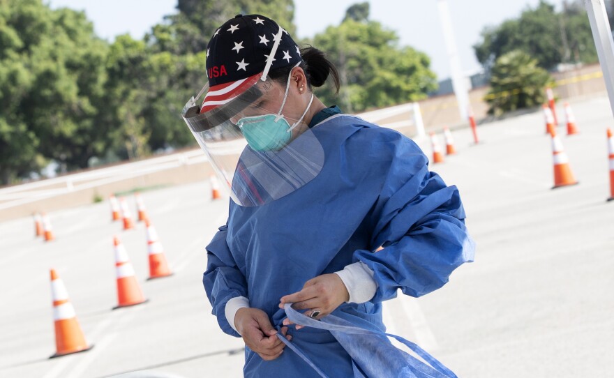 A health worker dons protective gear at a drive-through COVID-19 testing site set up by the Los Angeles Fire Department in Inglewood, Calif., on Monday. The Trump administration has released new guidelines on testing.