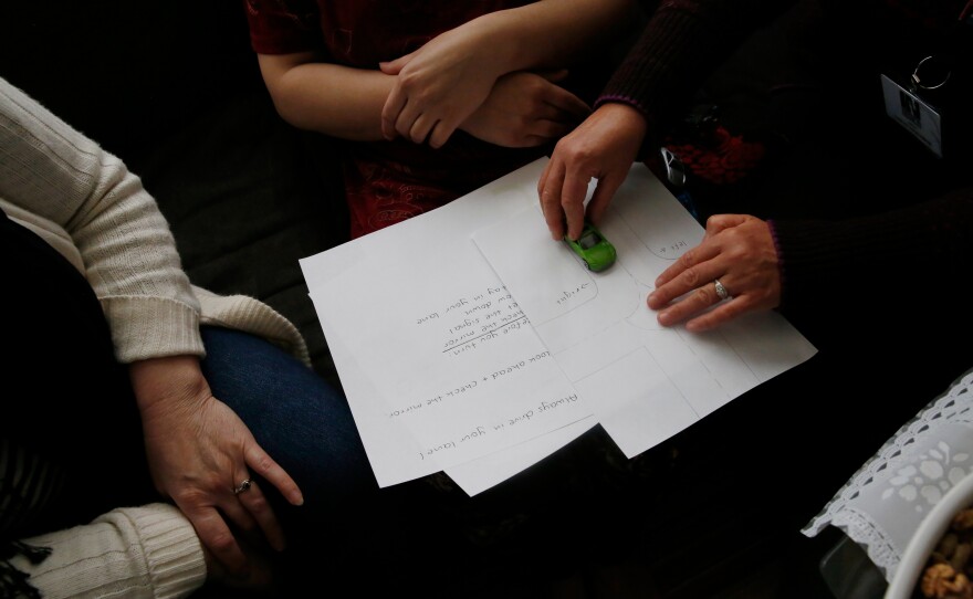 Helga Hiss gives a driving lesson using a metal toy car and a piece of white paper with lines that represent a T-shaped intersection.