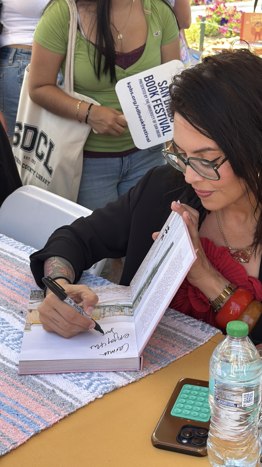 Chef and author Claudette Zepeda signs a copy of her cookbook, "Cooking the Borderlands: Spice and Smoke Between Mexico and the States," during the 2026 KPBS San Diego Book Festival at the University of San Diego on Aug. 22, 2026.
