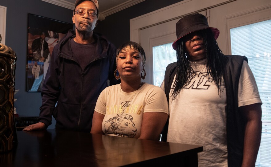 Ebony Everson (center), Bobby Everson's sister, stands with her father, who is also named Bobby Everson, and her mother Sabrina Everson. Photos of their son Bobby are on the wall behind them.