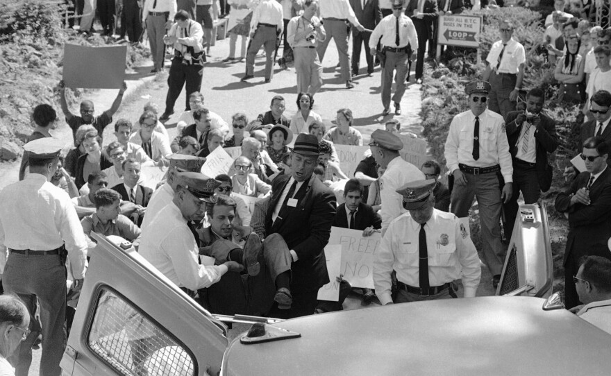 Baltimore County police officers lift a white demonstrator into a patrol wagon on July 4, 1963. The man was arrested after he and some 400 other demonstrators protested the whites-only policy of Gwynn Oak Amusement Park in suburban Woodlawn, Md. Other demonstrators who had been arrested and escorted from the park sit in the background.