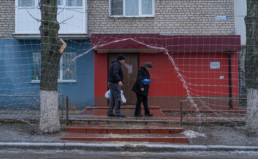Civilians walk along Izium's city streets where nets overhang.