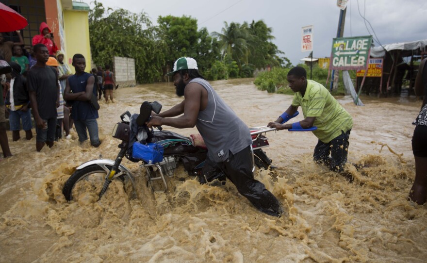 Men push a motorbike through a flooded street in Leogane, Haiti. U.N. peacekeepers already in Haiti spent Wednesday trying to clear local roads around Port-au-Prince.